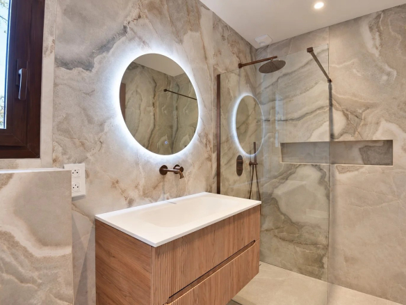 Salle de bain moderne avec douche à l'italienne et miroir rond lumineux.