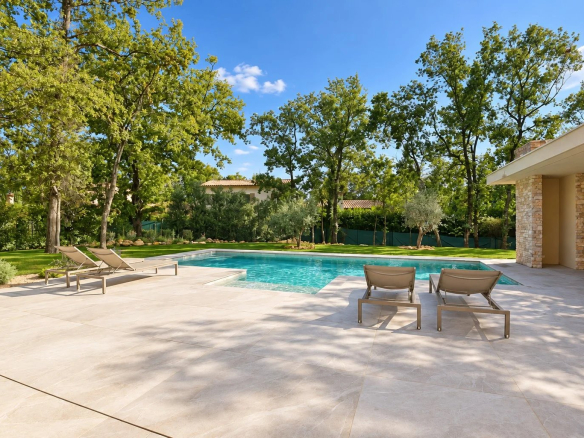 Villa contemporaine avec piscine et chaises longues, entourée d'arbres dans un jardin.