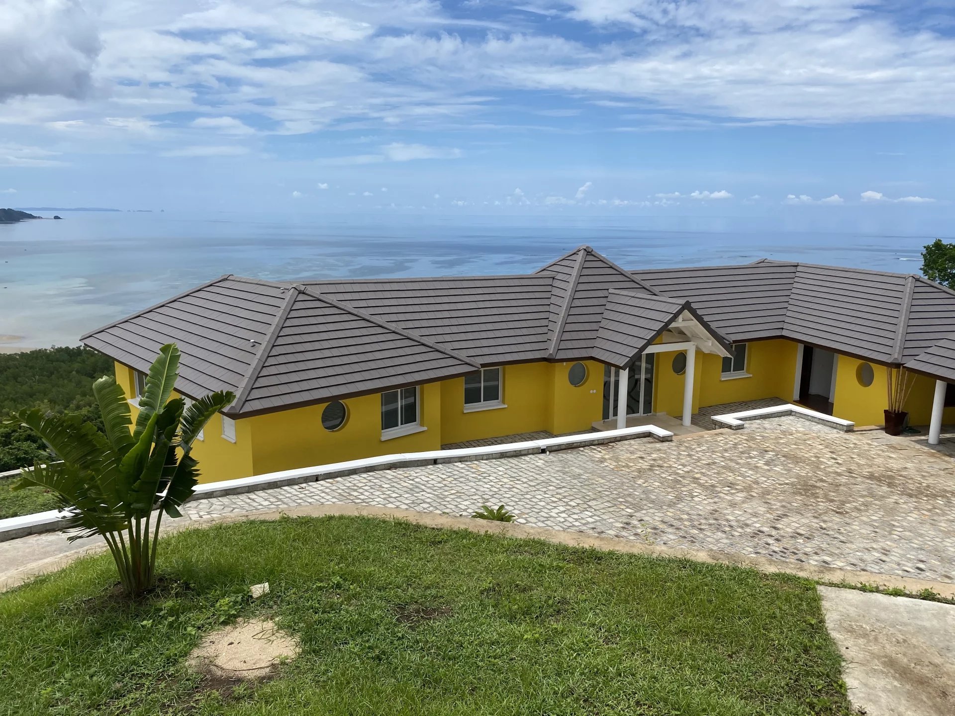 Villa à vendre à Nosy Be Villa jaune avec vue sur l'océan à Nosy Be, Madagascar, entourée de verdure.