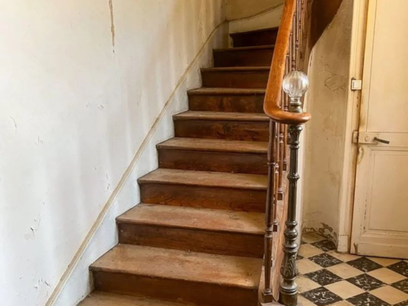 Escalier en bois menant à l'étage, avec un garde-corps en métal, dans un bâtiment ancien.