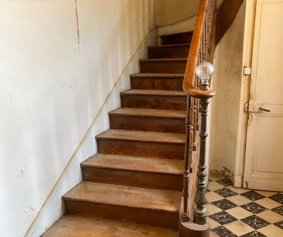 Escalier en bois menant à l'étage, avec un garde-corps en métal, dans un bâtiment ancien.
