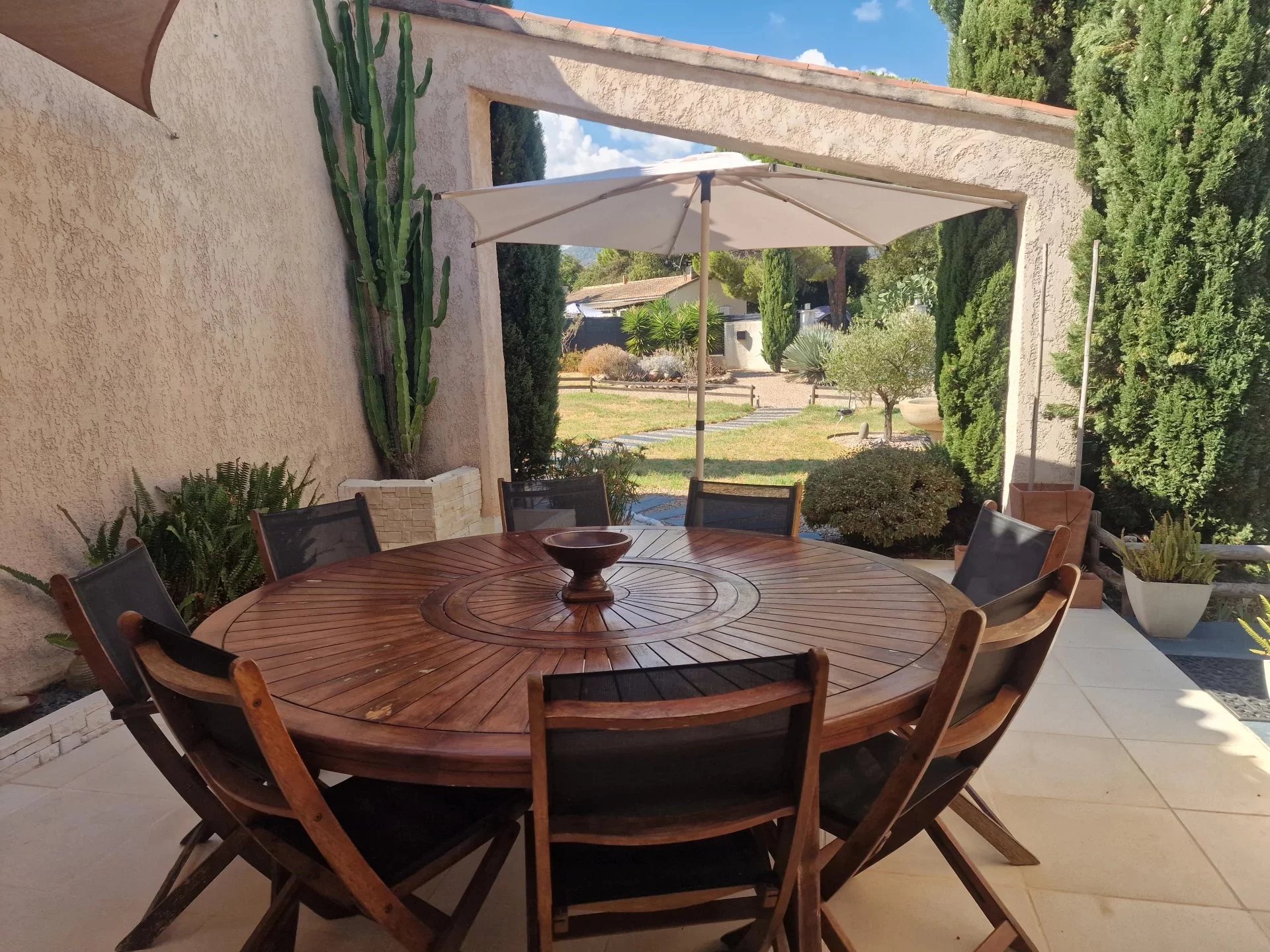 Terrace of the villa at the Marine de Solaro Outdoor terrace with round wooden table and chairs, surrounded by greenery at the Marine de Solaro in Corsica.