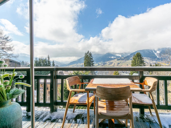Terrasse d'un appartement avec vue sur les montagnes à Megève, mobilier en bois et décoration florale.