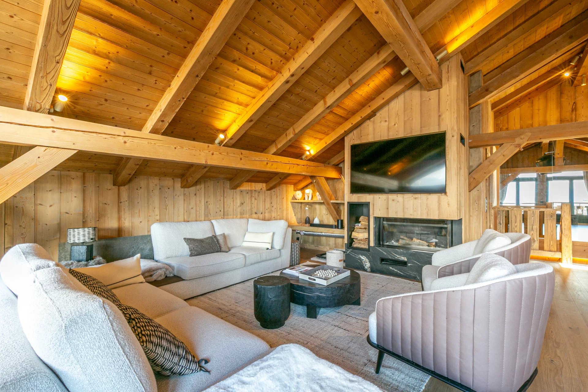 Salon d’un appartement de prestige à Megève Salon spacieux avec poutres apparentes et cheminée dans un appartement à Megève.