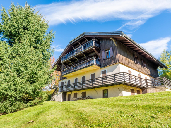 Vue extérieure d'un appartement en bois à Megève avec jardin et arbres.