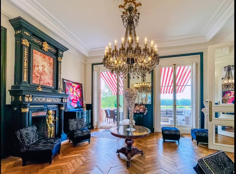 Intérieur d'un château avec un lustre, des fauteuils et des fenêtres à rideaux rayés.