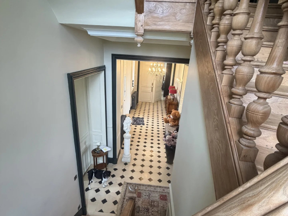 Escalier en bois menant à un hall d'entrée d'un château avec un sol en damier noir et blanc.