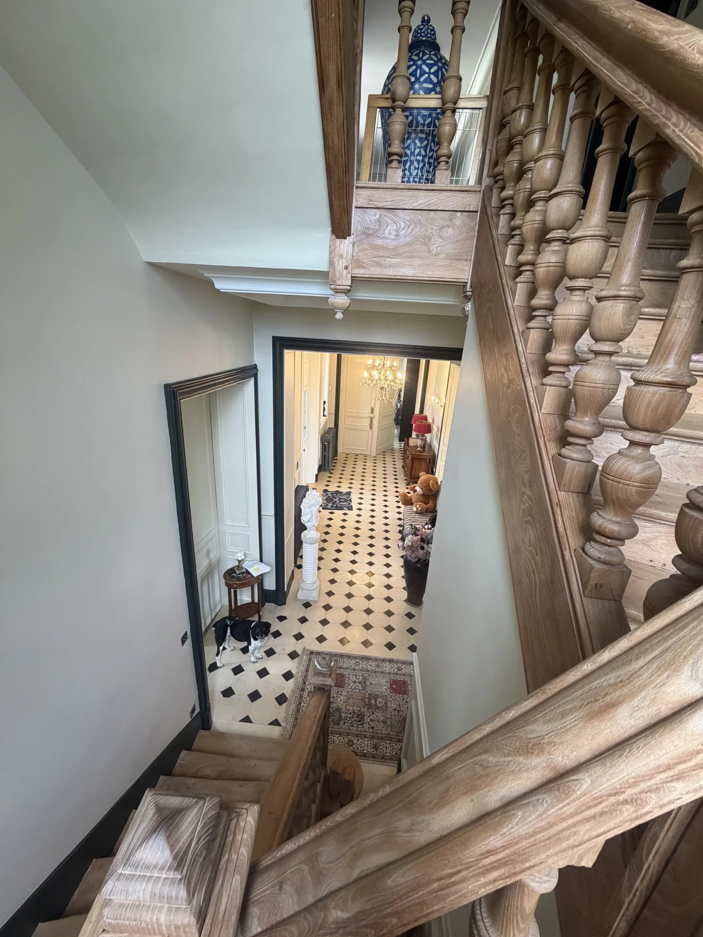 Escalier en bois menant à un hall d'entrée d'un château avec un sol en damier noir et blanc.
