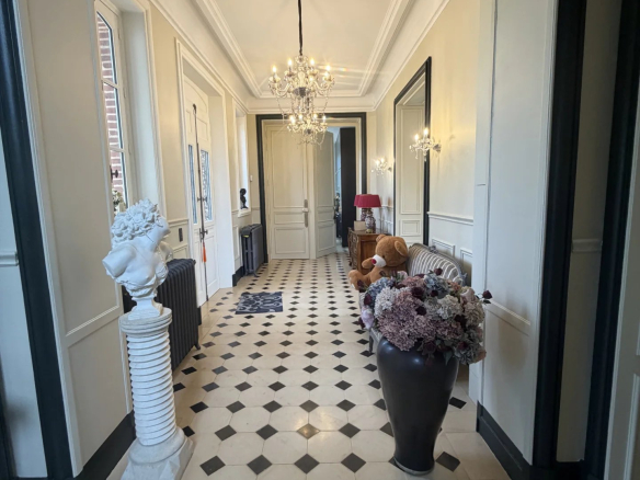 Intérieur d'un château avec un couloir décoré de carrelage noir et blanc, éclairé par un lustre.
