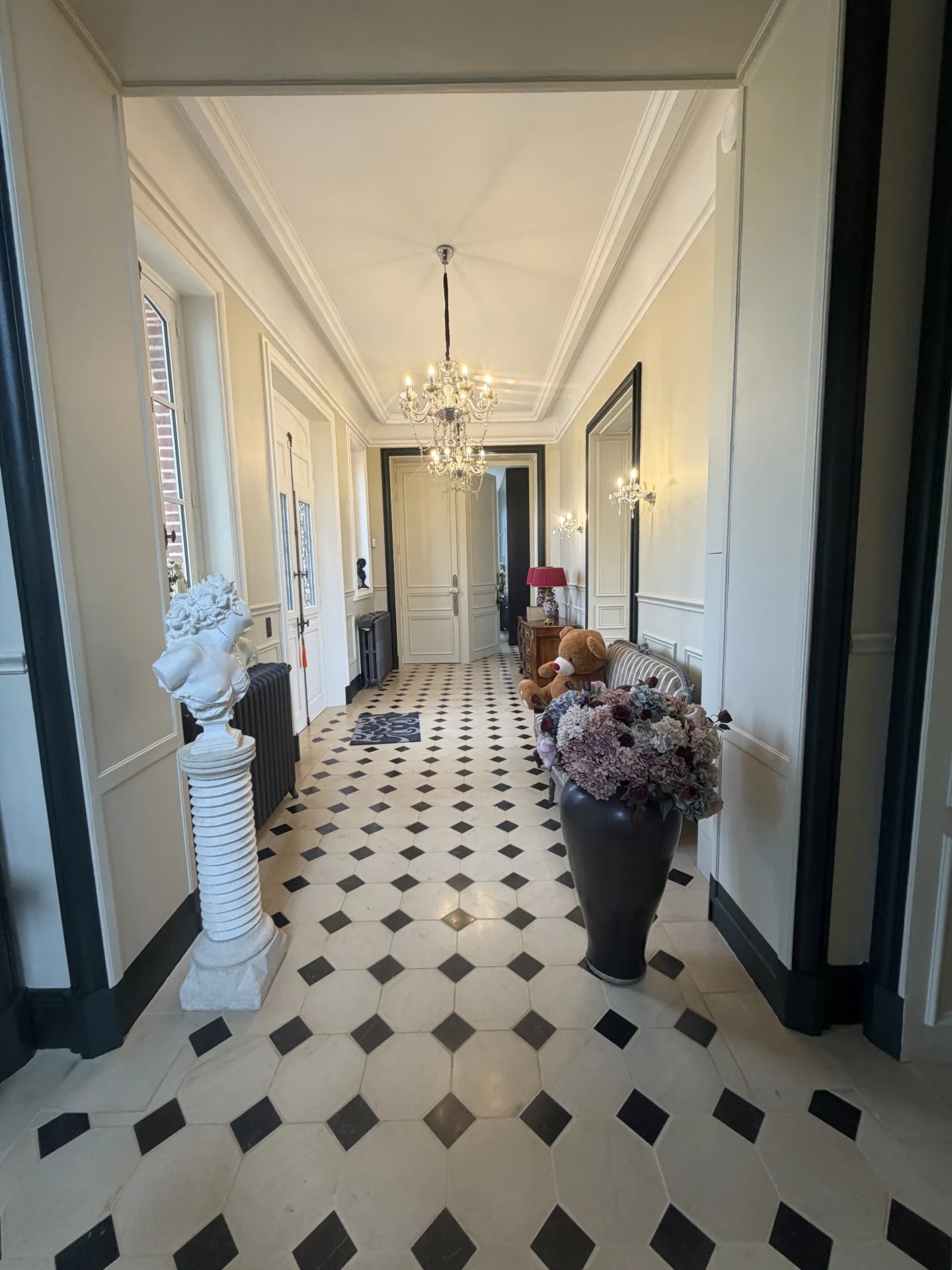 Intérieur d'un château avec un couloir décoré de carrelage noir et blanc, éclairé par un lustre.