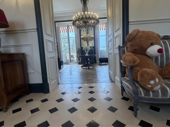 Intérieur d'un château avec un sol en carreaux noirs et blancs, un lustre et un ours en peluche sur une chaise.