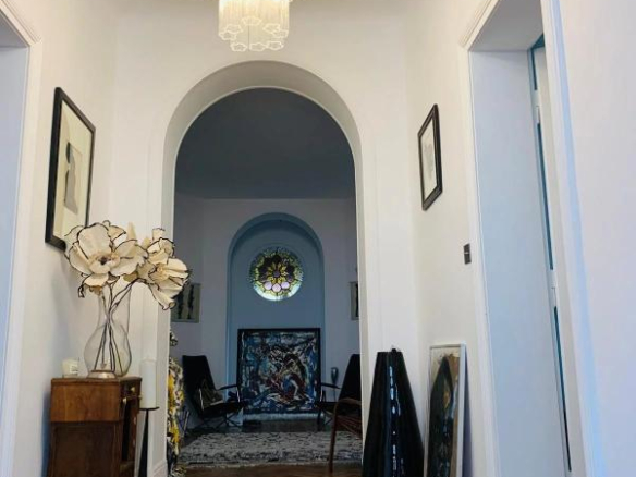 Bright entry hall with a large crystal chandelier, white walls, and an arched doorway opening to a room with a circular stained-glass window.