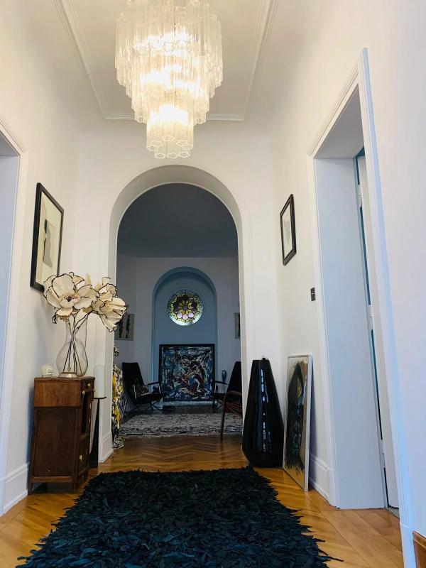 Bright entry hall with a large crystal chandelier, white walls, and an arched doorway opening to a room with a circular stained-glass window.