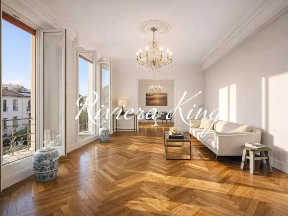 Bright living room with tall windows, herringbone wooden floor, and a crystal chandelier above a cream sofa set.