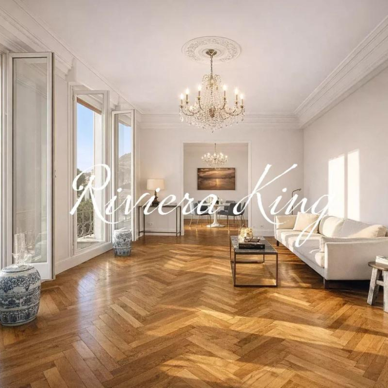 Bright living room with tall windows, herringbone wooden floor, and a crystal chandelier above a cream sofa set.