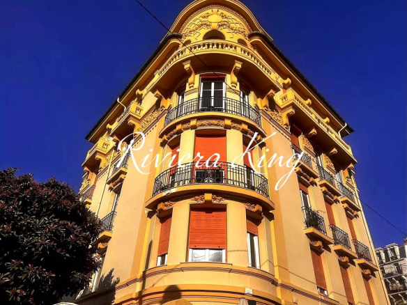 Yellow ornate corner apartment building with curved balconies, red shutters, and decorative details against a clear blue sky.