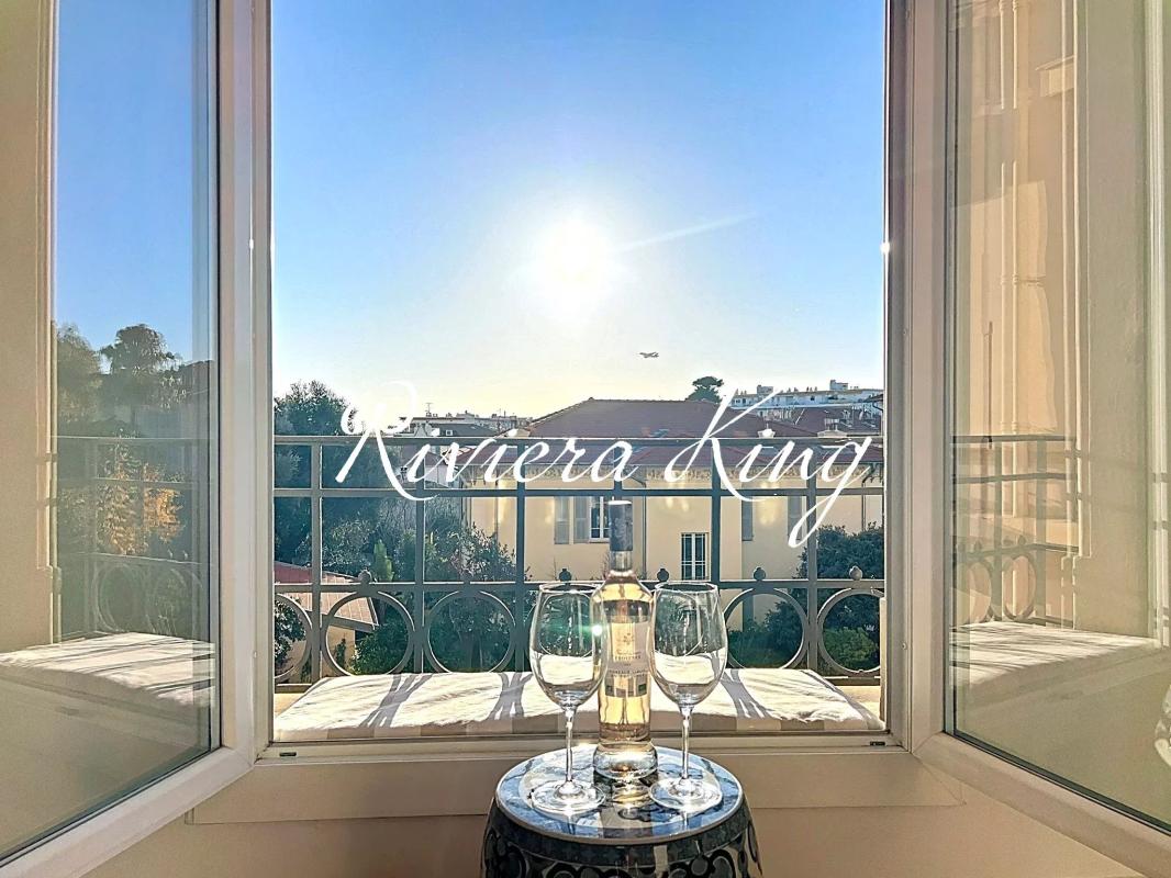 Sunlit balcony scene with a bottle of white wine and two empty glasses on a small table by an open window.