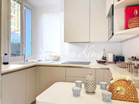 Bright white modern kitchen with a windowed sink area and a white table in the foreground set with striped cups and a decorative pineapple jar centerpiece.