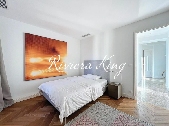 Bedroom with white bedding and gray headboard, large orange abstract artwork on the wall, and a small nightstand by the bed.
