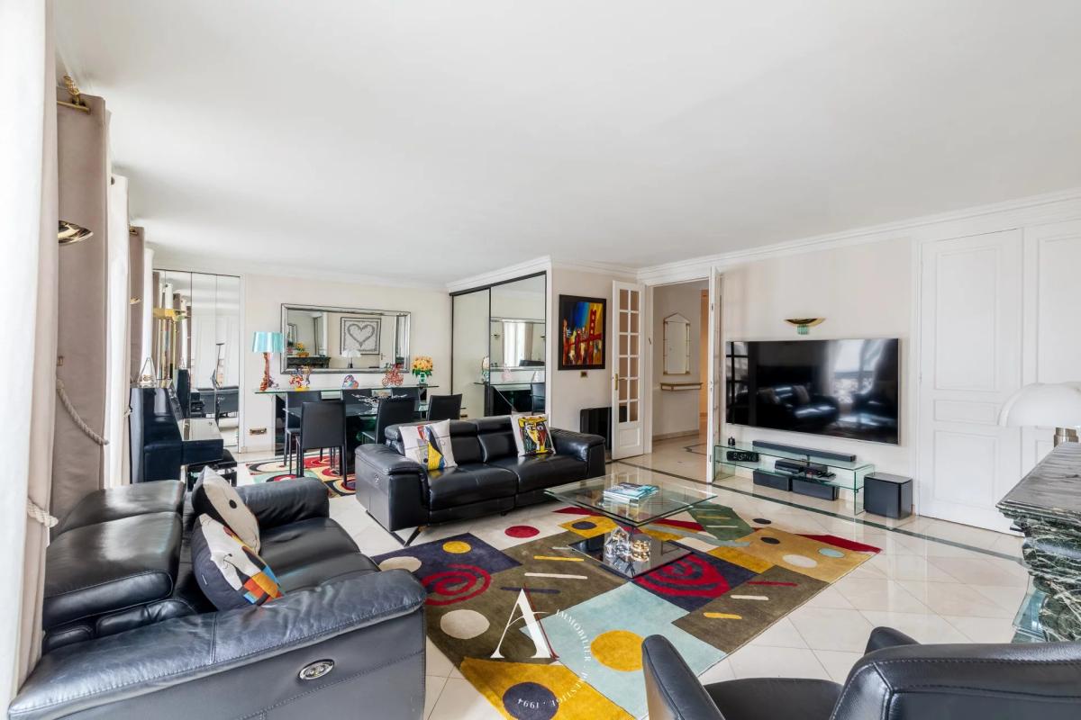 Open-concept living room with black leather sofas, glass coffee table, and a colorful geometric rug facing a wall-mounted TV.