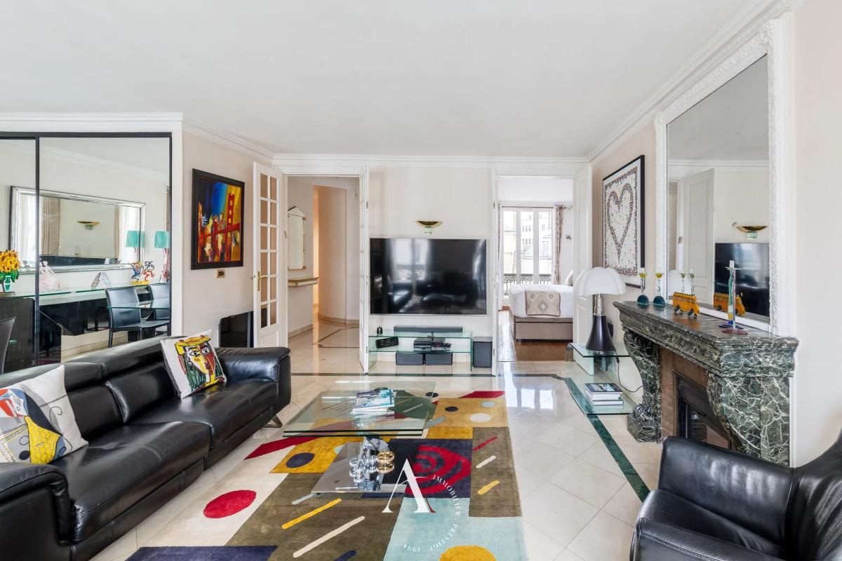 Bright, contemporary living room with black leather sectional, glass coffee table, and a colorful abstract rug.
