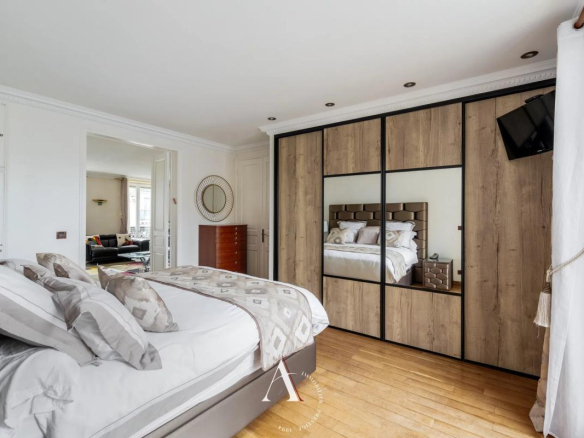 Bright bedroom with a large wooden wardrobe featuring mirrored doors and white linens on a low bed.