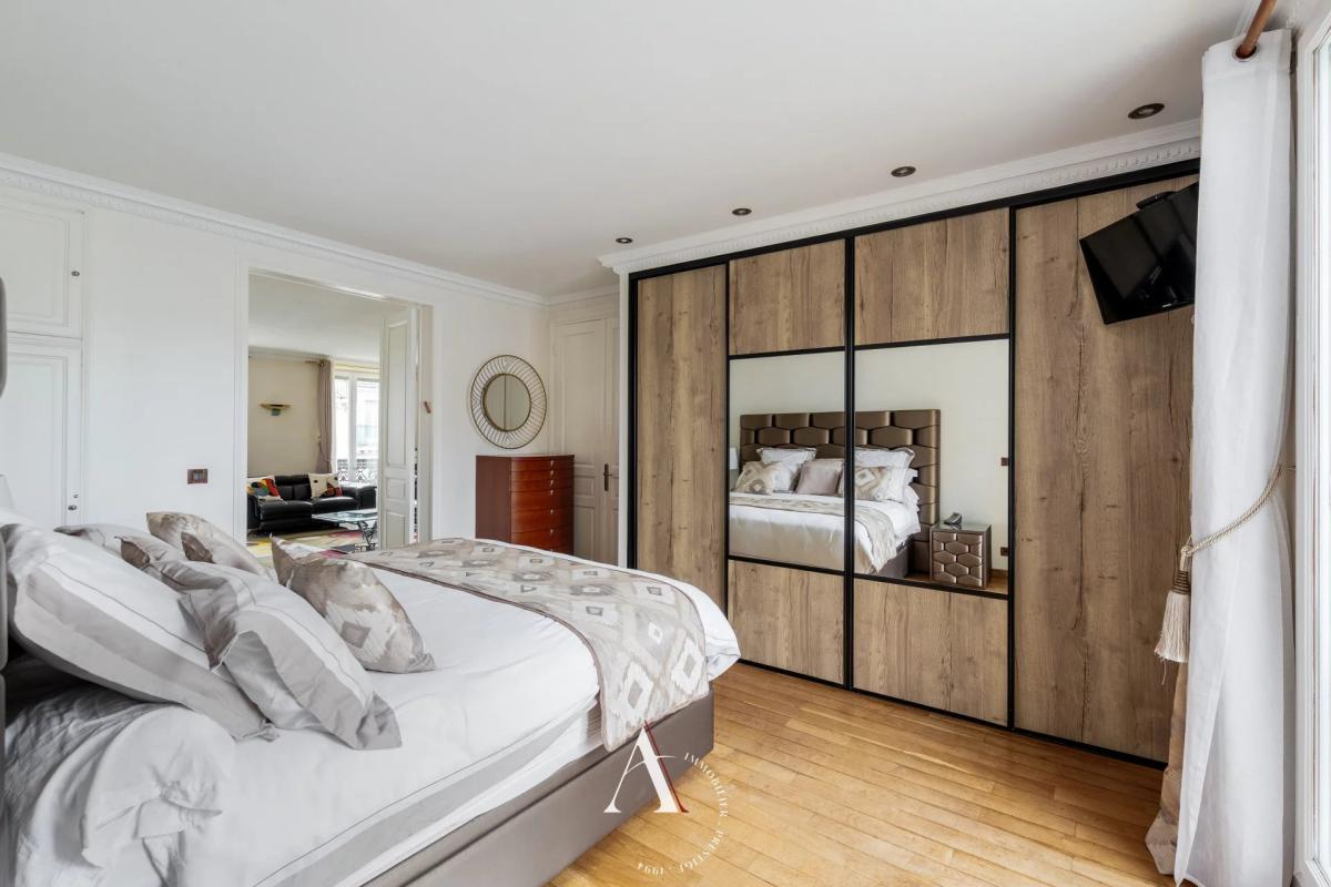 Bright bedroom with a large wooden wardrobe featuring mirrored doors and white linens on a low bed.