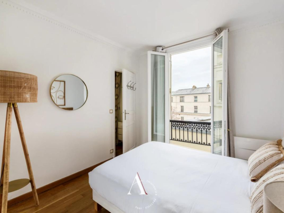 Bright white bedroom with open French balcony doors, showing a city view and an iron railing outside.