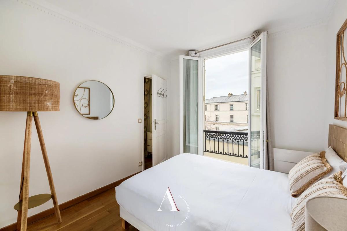 Bright white bedroom with open French balcony doors, showing a city view and an iron railing outside.