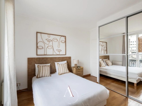 Bright bedroom with a white duvet, brown tufted headboard, and two striped pillows beneath an abstract line-art portrait above the bed.