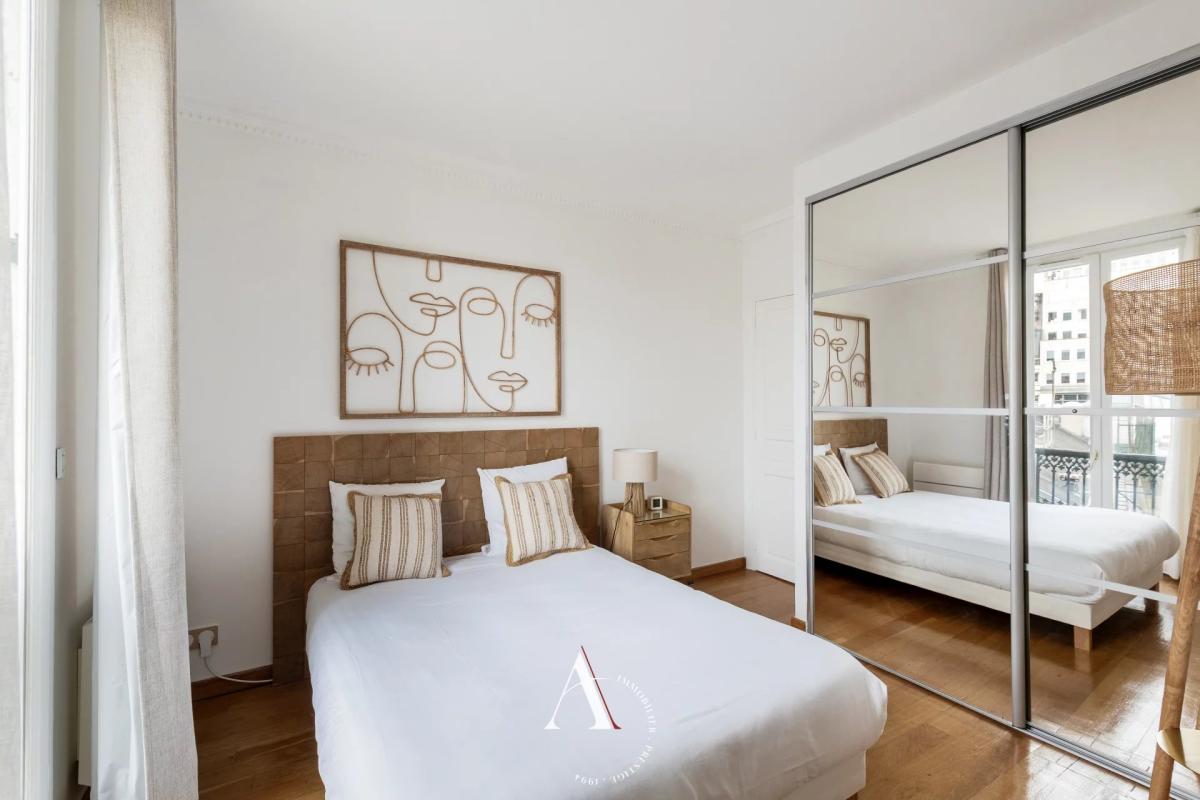 Bright bedroom with a white duvet, brown tufted headboard, and two striped pillows beneath an abstract line-art portrait above the bed.