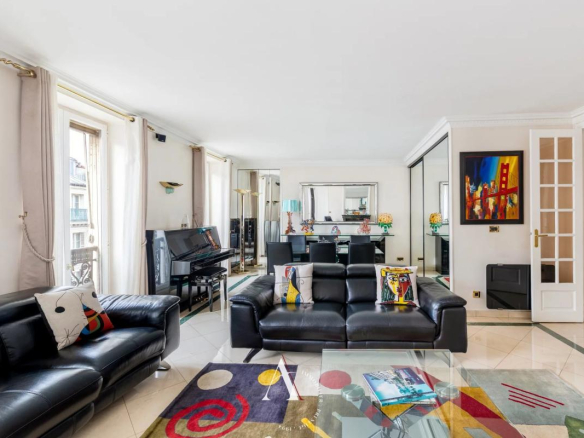 Bright contemporary living room with black leather sofas, colorful cushions, a glass coffee table, and a piano by the windows.