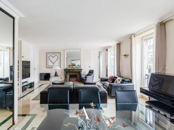 Bright living room with glass dining table, butterfly centerpiece, black leather sofas, piano, and a fireplace in the center.