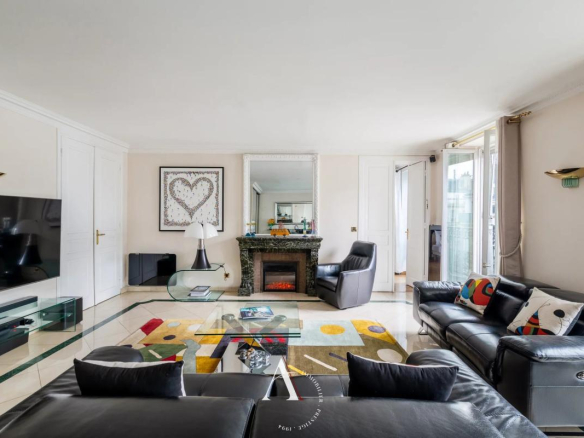 Bright living room with black leather sofas, glass coffee table, colorful rug, and a marble fireplace in a bright open plan space.