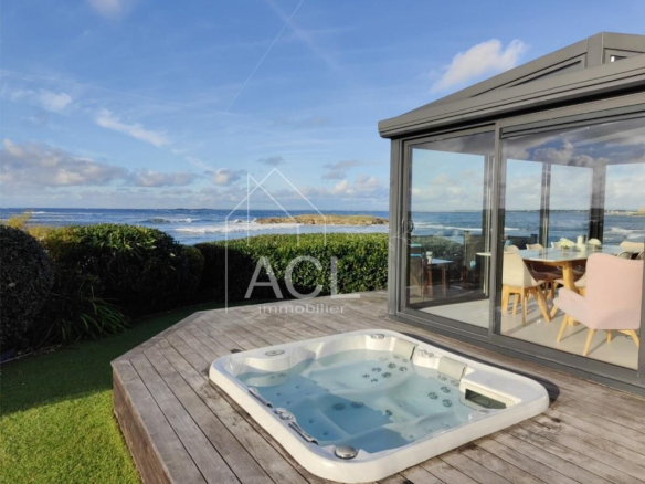 Outdoor deck with a hot tub, overlooking the sea and a glass-walled dining area.