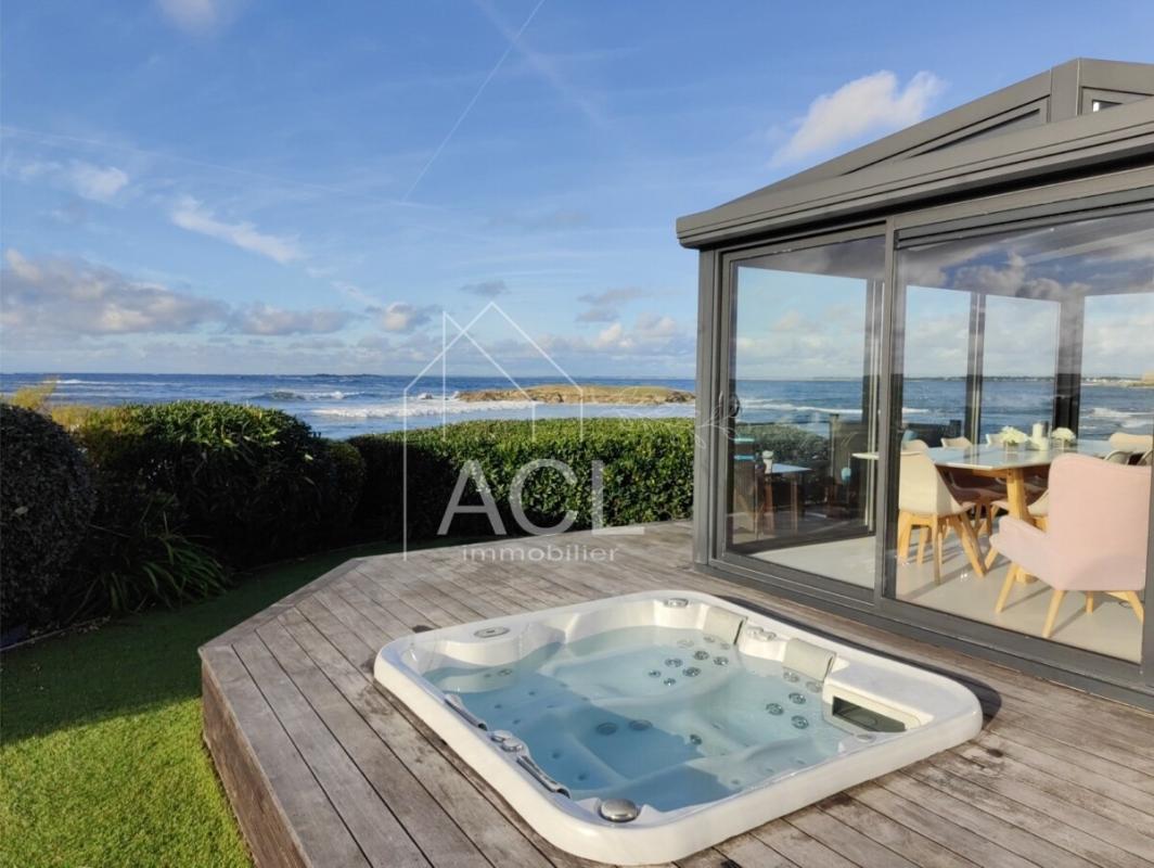 Outdoor deck with a hot tub, overlooking the sea and a glass-walled dining area.