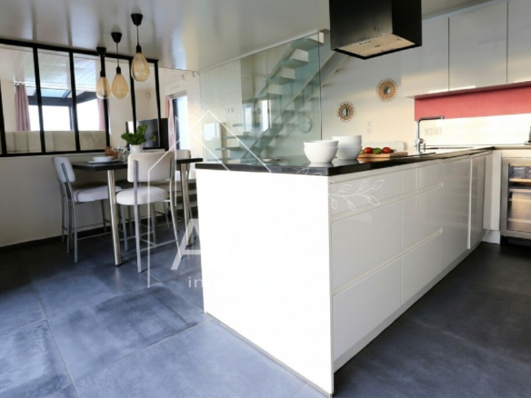 Bright contemporary kitchen with a white island, dark countertop, and a glass-walled dining area in the background.