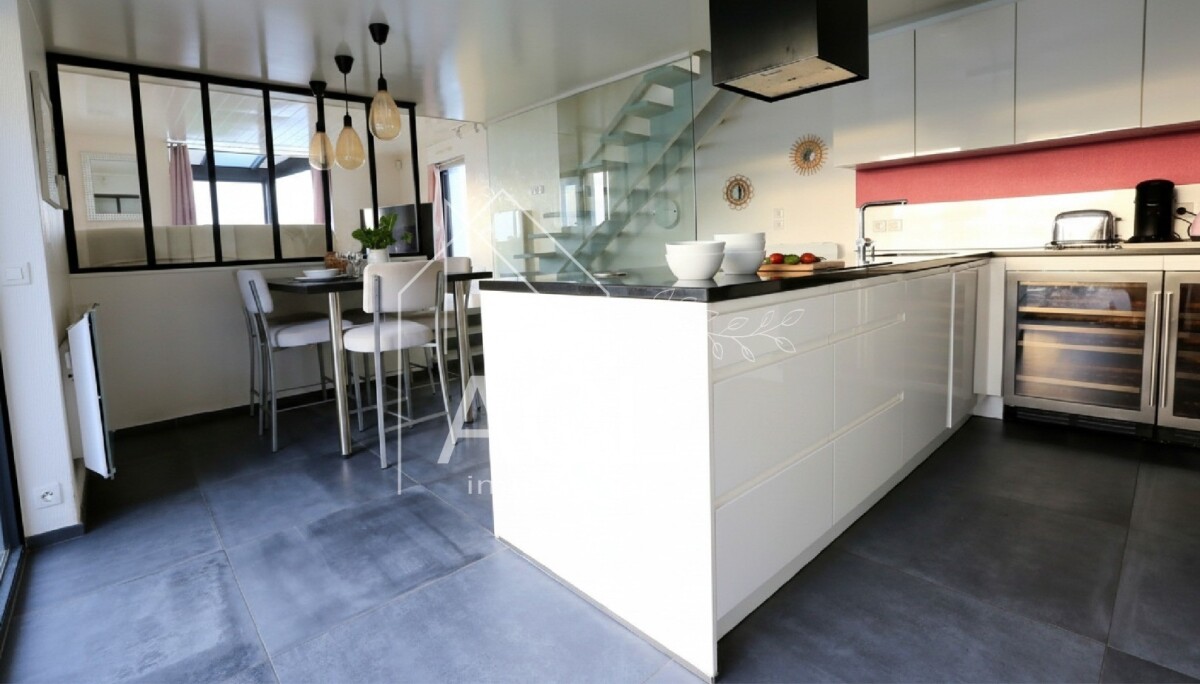 Bright contemporary kitchen with a white island, dark countertop, and a glass-walled dining area in the background.
