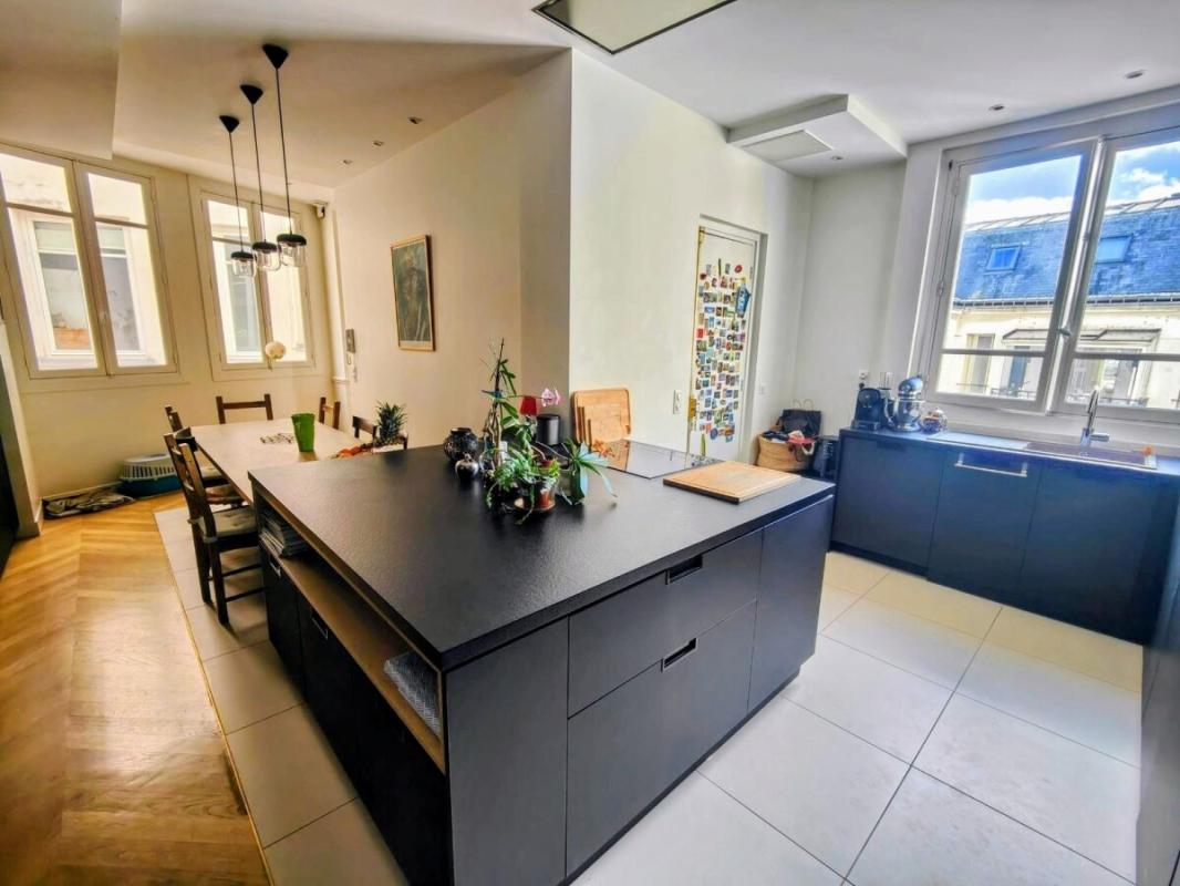 Modern kitchen with a large black island, potted plants, and a dining table nearby.
