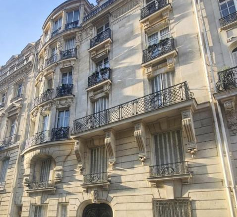 Haussmann-style stone apartment building with ornate balconies and arched windows on a sunny street corner.