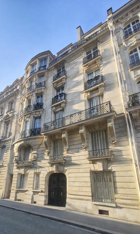 Haussmann-style stone apartment building with ornate balconies and arched windows on a sunny street corner.