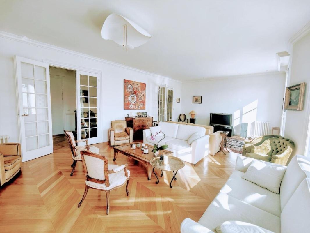 Bright living room with white sofas, vintage armchairs, glass coffee tables, and French doors opening to another room.