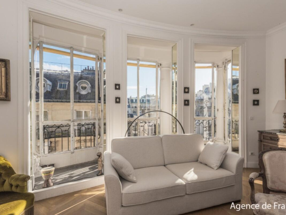 Bright Parisian living room with large bay windows and a beige sofa facing an urban balcony view