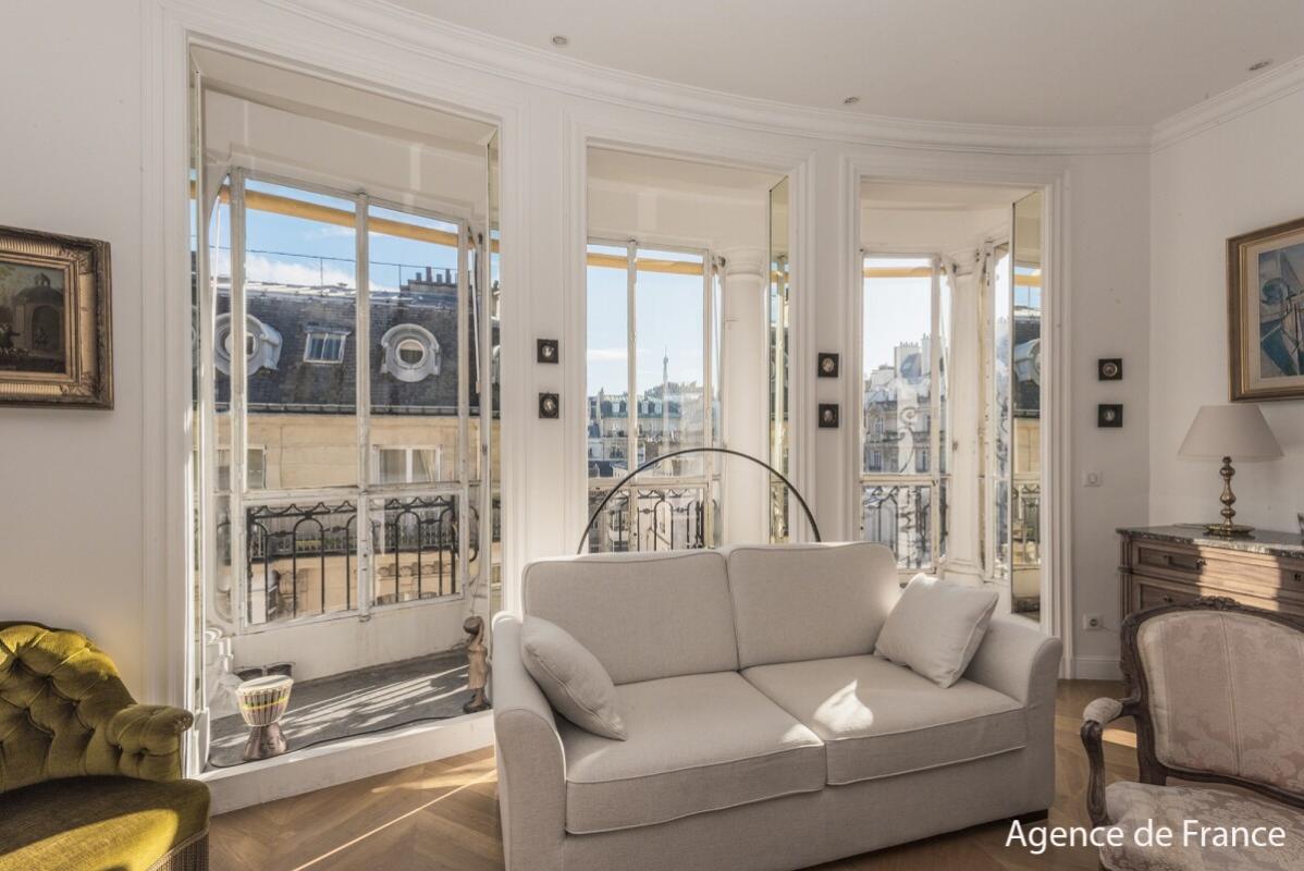Bright Parisian living room with large bay windows and a beige sofa facing an urban balcony view