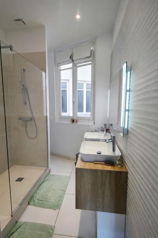 Modern bathroom with a glass shower enclosure, a wood vanity with two white vessel sinks, a large window, and mint-green bath mats.
