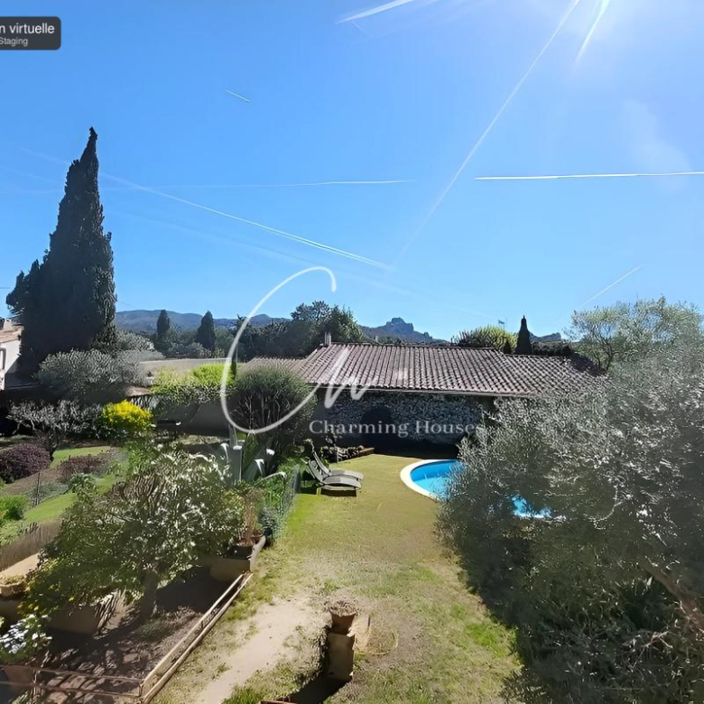 Sunlit backyard with a curved blue pool, a tiled-roof house, and a manicured garden of shrubs and trees under a bright blue sky with contrails.