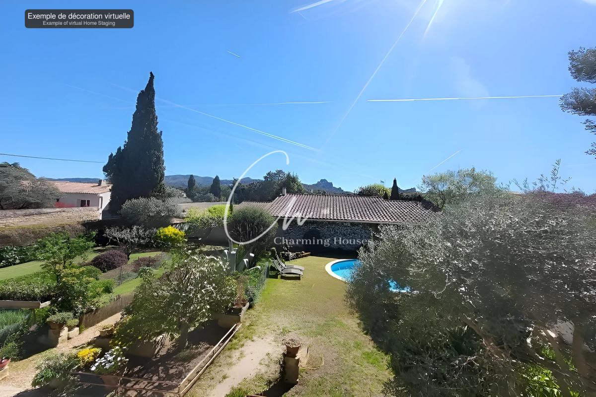 Sunlit backyard with a curved blue pool, a tiled-roof house, and a manicured garden of shrubs and trees under a bright blue sky with contrails.