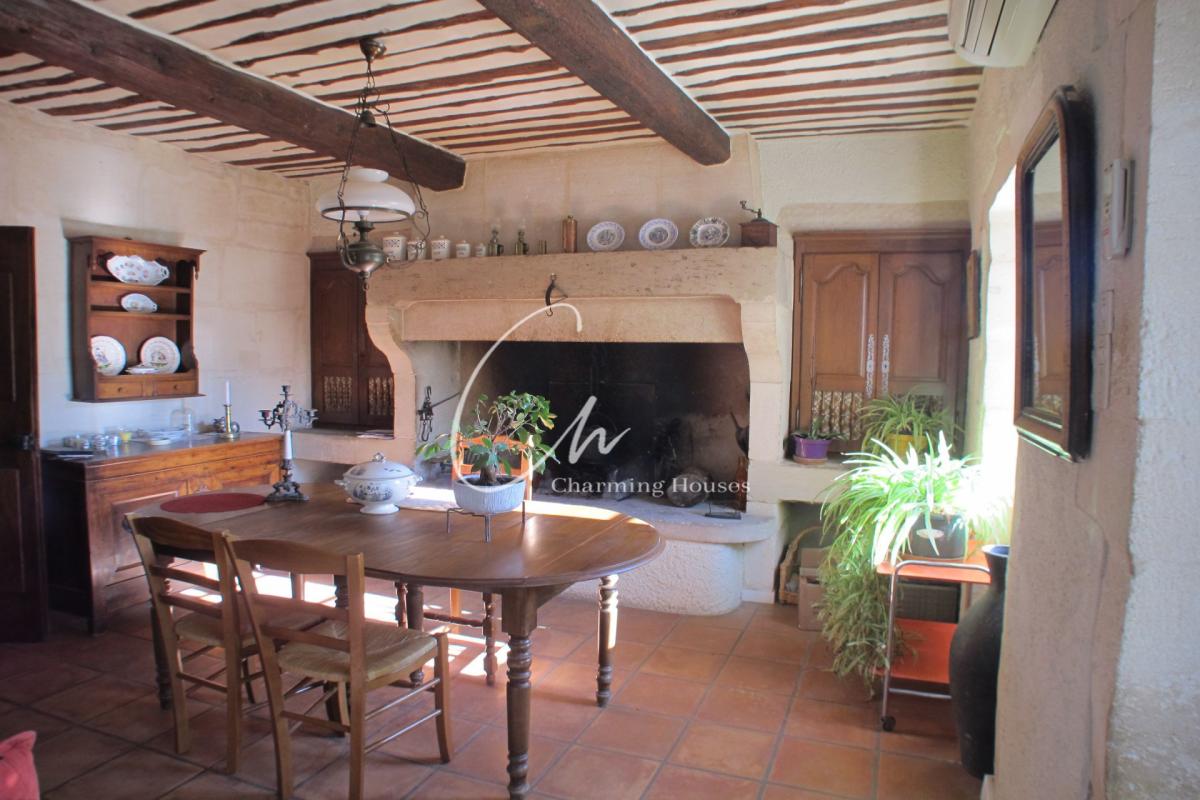 Rustic dining room with a large stone fireplace, wooden beams, and terracotta-tiled floor; a wooden table and chairs sit beneath a hanging lamp.