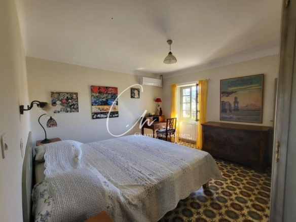 A cozy bedroom with a large bed covered in a white quilt, wood nightstands, and patterned tiled floor, sunlight streaming through a window with yellow curtains.