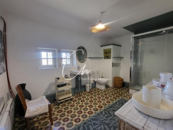 Rustic bathroom with patterned tile floor, white walls, pedestal sink, toilet, and glass shower stall with vintage decor.